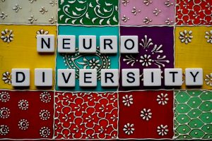 the word neurodiversity is spelled out using letter tiles. The letter tiles are arranged over an array of colourful patterned ceramic tiles.