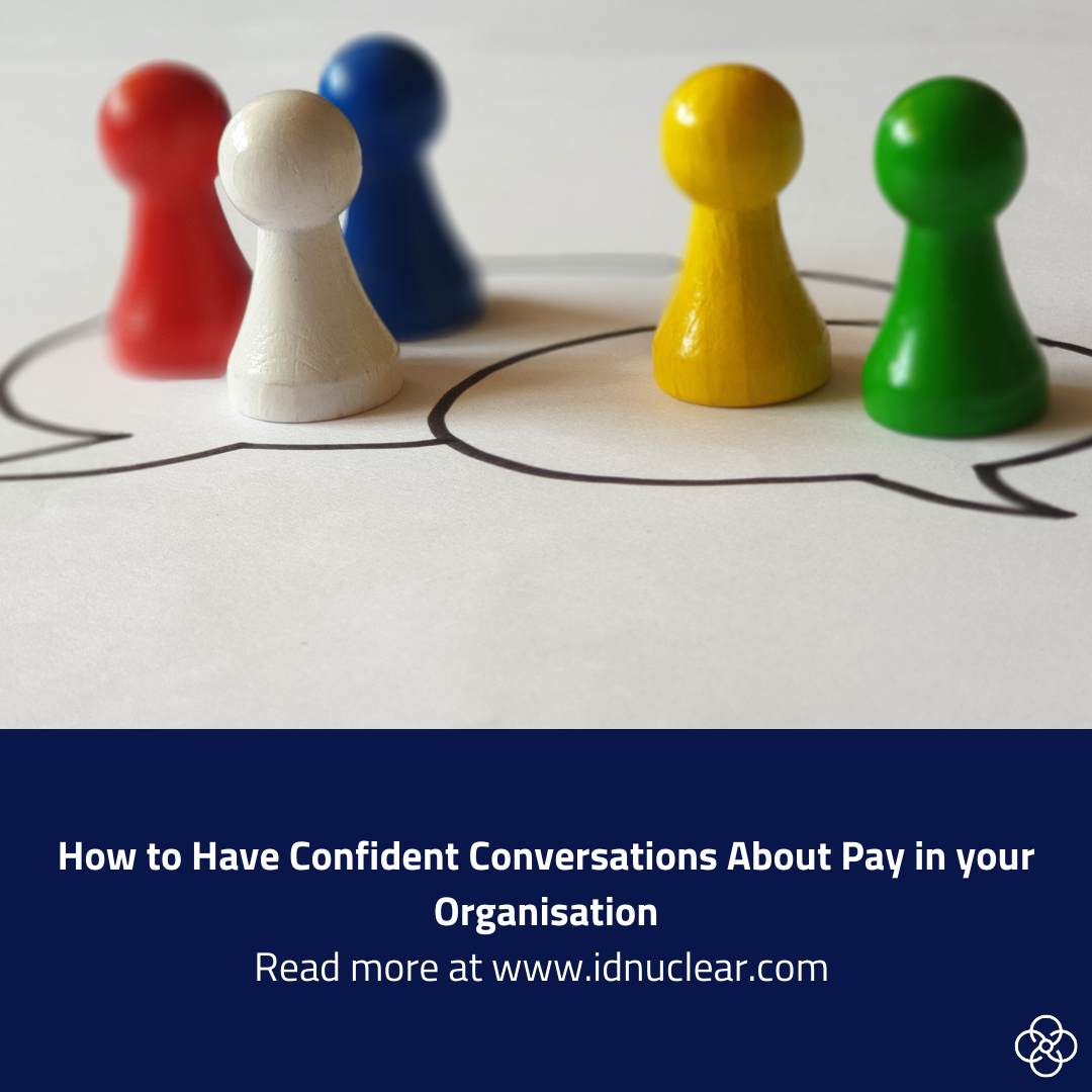 Five coloured wooden figures arranged in two groups on a white background, suggesting discussion or separation. Text reads: ‘How to Have Confident Conversations About Pay in your Organisation’.
